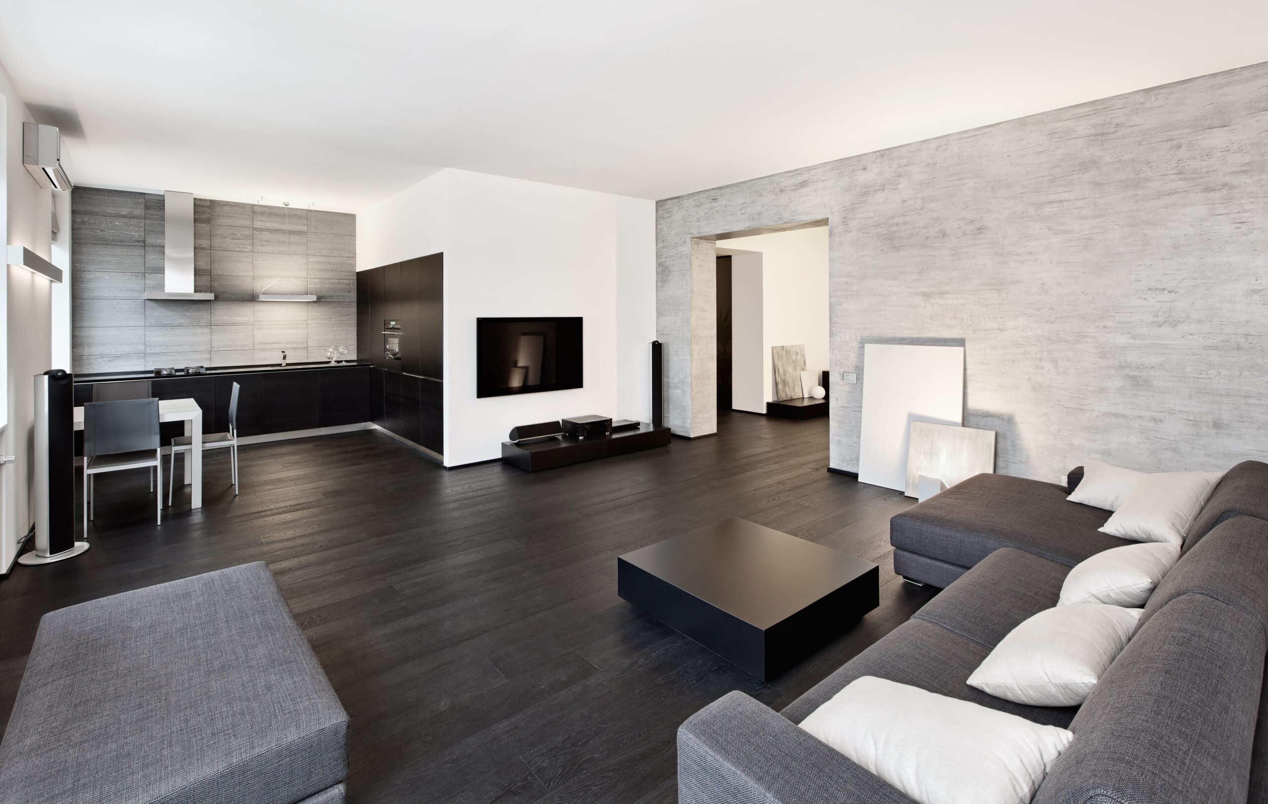 Modern living room featuring a sleek sofa, minimalist coffee table, and a contemporary kitchen in black and gray tones.