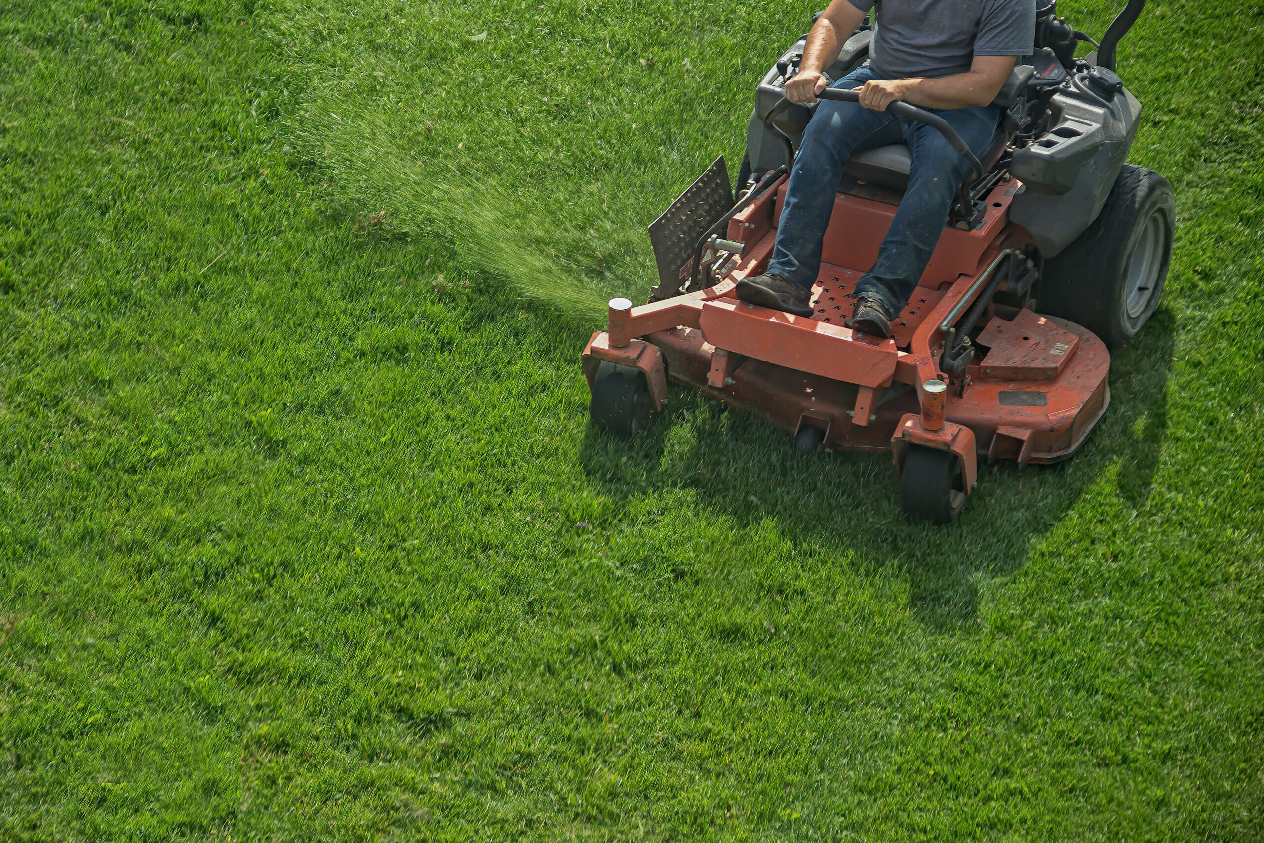 A person operates a riding lawn mower, applying fertilizer to a lush green lawn, illustrating lawn care maintenance.