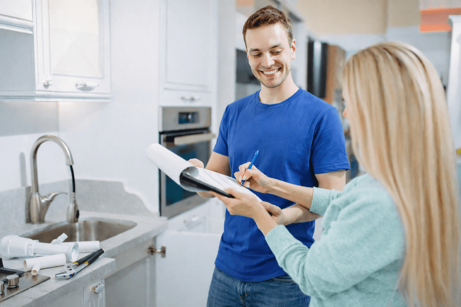 A contractor and a client discuss home renovation plans in a modern kitchen, with tools and materials visible on the counter.