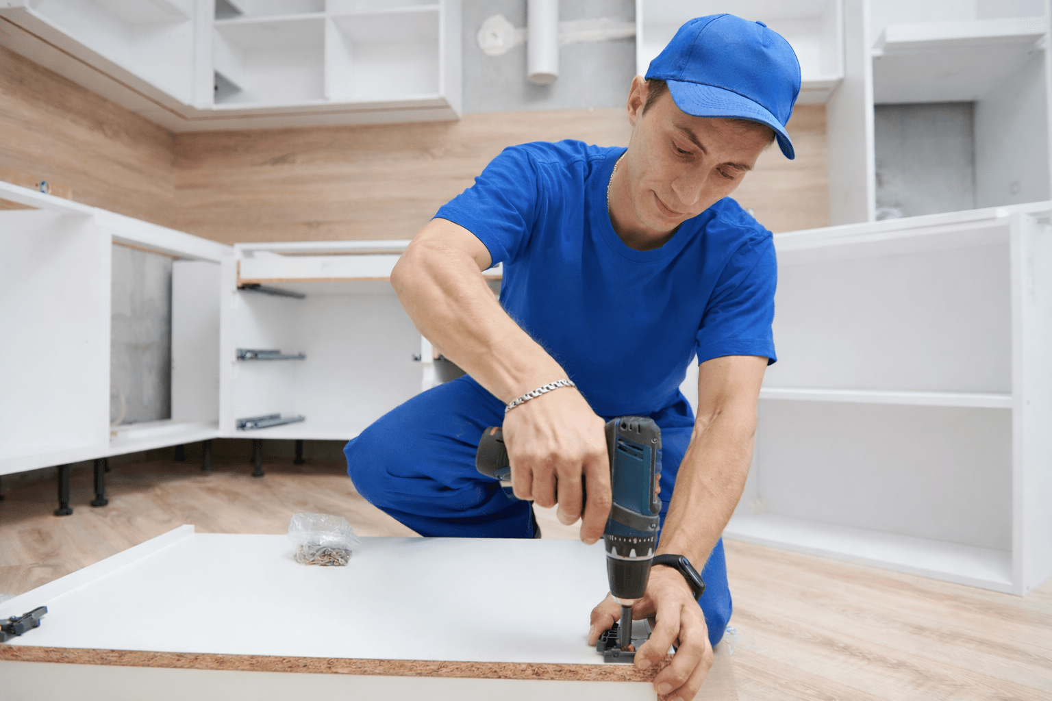 A man in blue attire uses a power drill to install a cabinet in a kitchen, showcasing hands-on skills for home improvement.