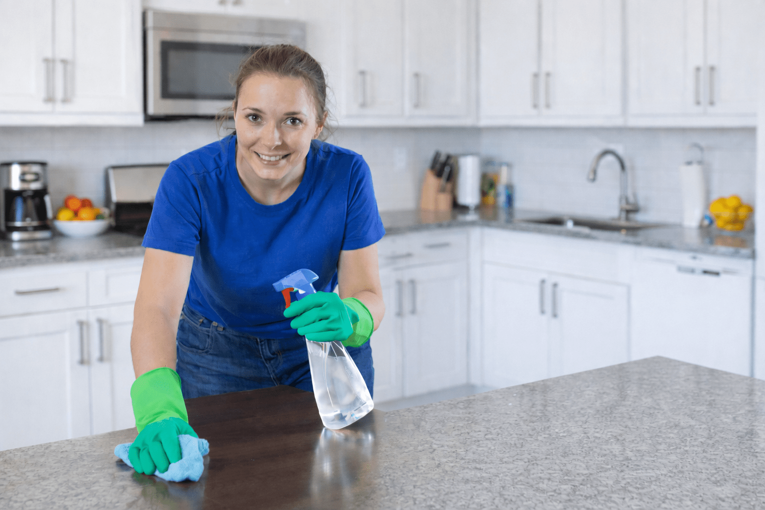 Woman cleaning a kitchen countertop with a spray bottle and cloth, emphasizing a neat and tidy home environment.