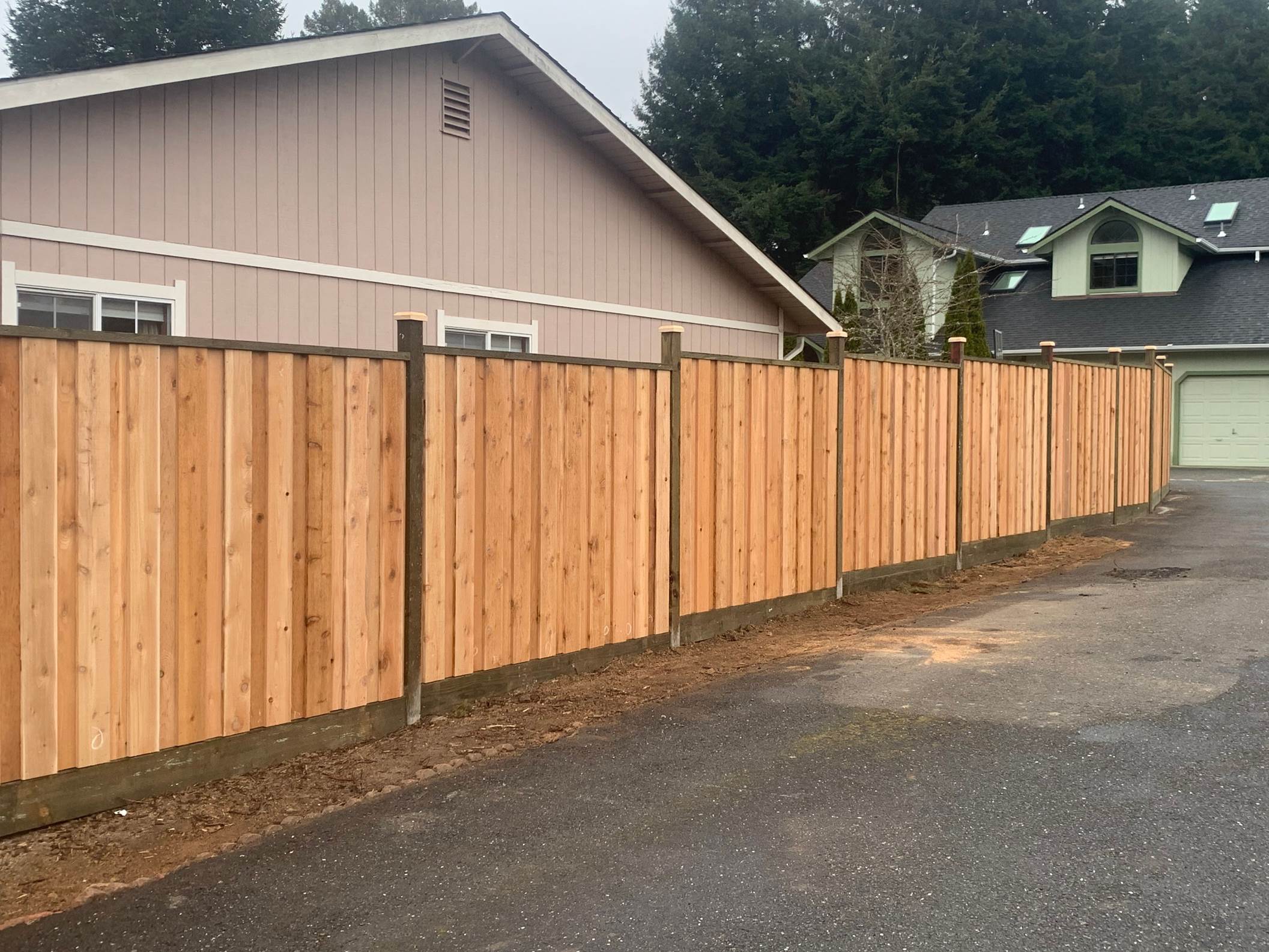 Wooden fence dividing residential properties, installed along a gravel driveway, showcasing a recently completed fencing project.