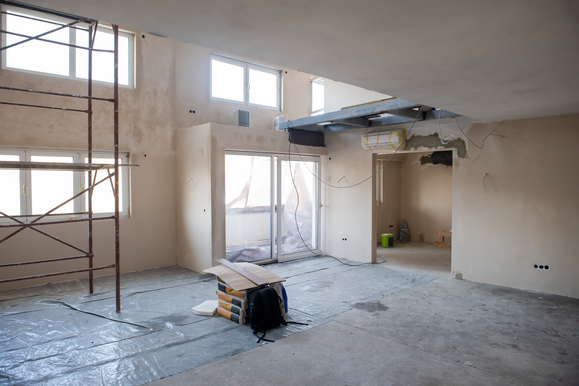 Renovated interior space under construction, featuring plastered walls, scaffolding, and construction materials scattered on the floor.